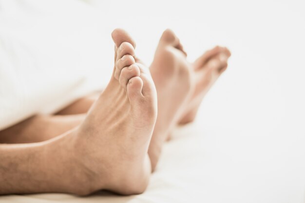 Pieds nus des amoureux sous couverture dans la chambre.