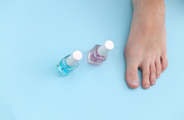 Pieds nus féminins, bouteille de vernis à ongles sur fond bleu. Concept de soins de beauté