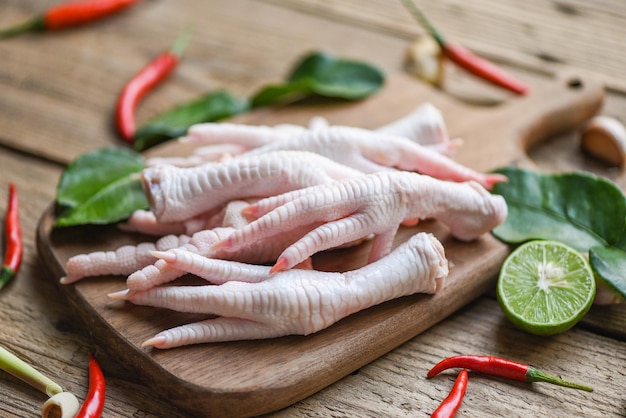 Pieds de poulet cru frais pour soupe de plats cuisinés sur le fond de la cuisine de la table sombre Pieds de poulet sur une planche à découper en bois avec des herbes et des épices citron piment ail kaffir feuilles de citron vert