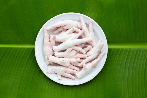 Pieds de poulet crus en plaque blanche sur fond de feuille de bananier