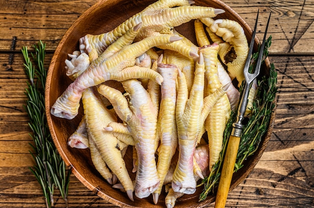 Pieds de poulet frais crus dans une assiette en bois.