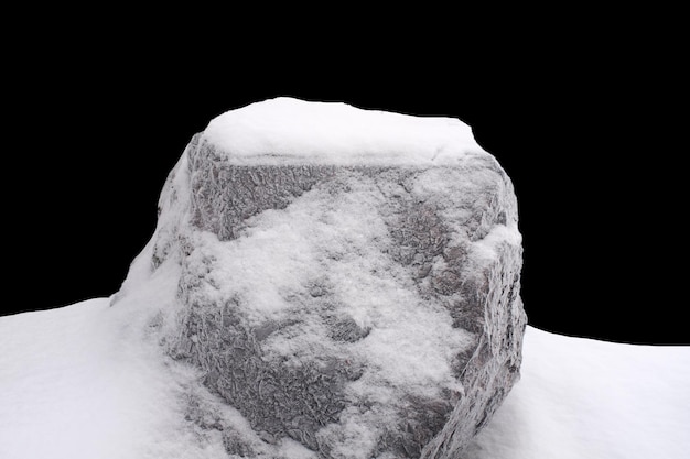 Pierre naturelle dans la neige isolée sur fond noir Photo de haute qualité