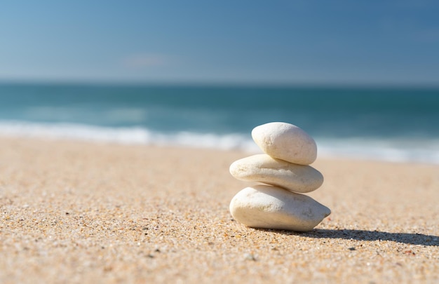 Des pierres blanches empilées sur le sable de la plage avec la mer bleue en arrière-plan.