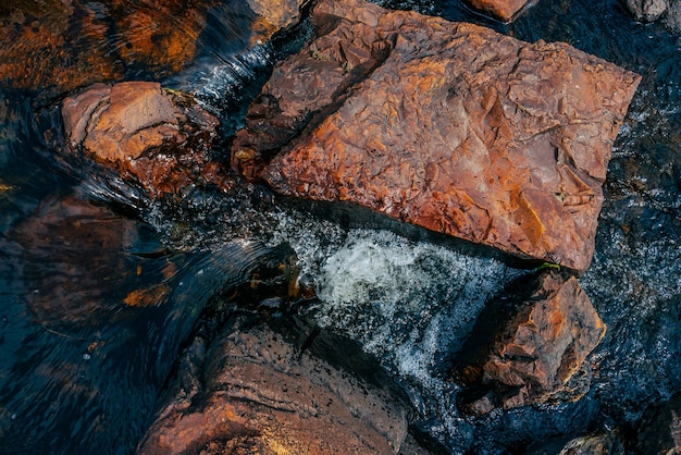 Pierres lisses en gros plan d'eau de source. L'eau propre s'écoule entre les pierres rouges et oranges.