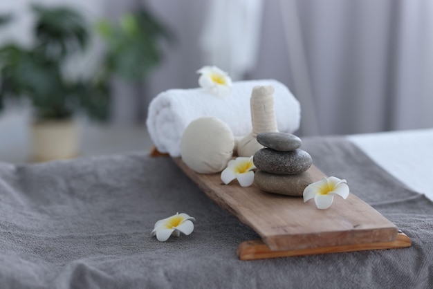 Des pierres de spa empilées, des fleurs, des sacs d'herbes et des serviettes sur la table de massage à l'intérieur.
