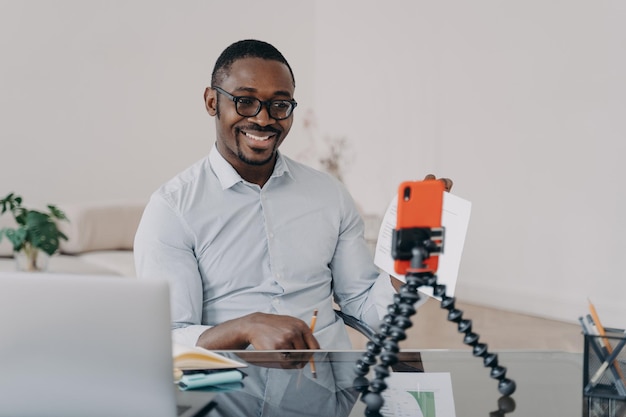 Un pigiste afro a un remue-méninges en ligne sur un smartphone Un homme heureux montre des documents avec des données