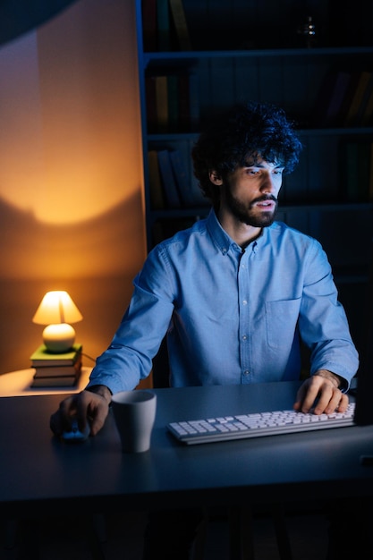 Un pigiste fatigué et épuisé regarde le moniteur et travaille en tapant sur un clavier sans fil tard dans la nuit. Concept de travail à distance, d'apprentissage à distance, de travail indépendant pendant la quarantaine du coronavirus.