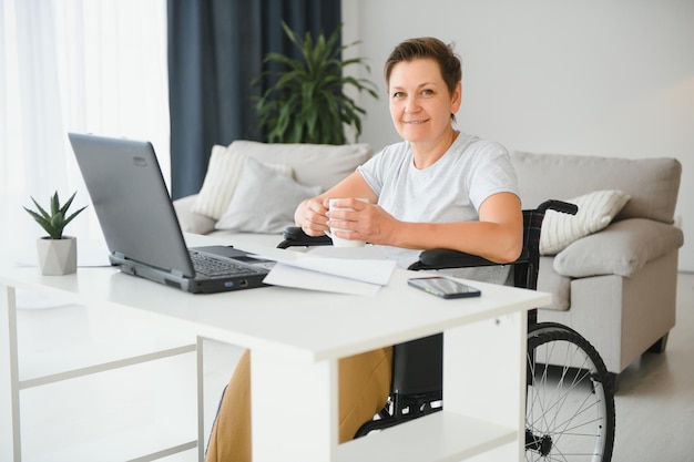 Pigiste en fauteuil roulant utilisant un ordinateur portable près d'un cahier et des papiers sur la table