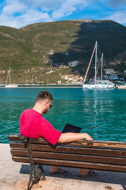 Pigiste homme travaillant sur ordinateur portable au banc du port de la ville l'été