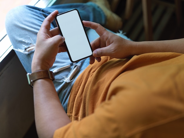 Pigiste mâle reposant avec écran blanc smartphone en position couchée détendue sur une chaise de bureau près de la fenêtre