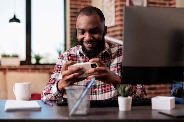 Pigiste masculin jouant à des jeux vidéo en ligne sur smartphone, travaillant à domicile. Utiliser un téléphone portable pour jouer à des compétitions de jeux sur le site Internet, s'asseoir à la maison et s'amuser.