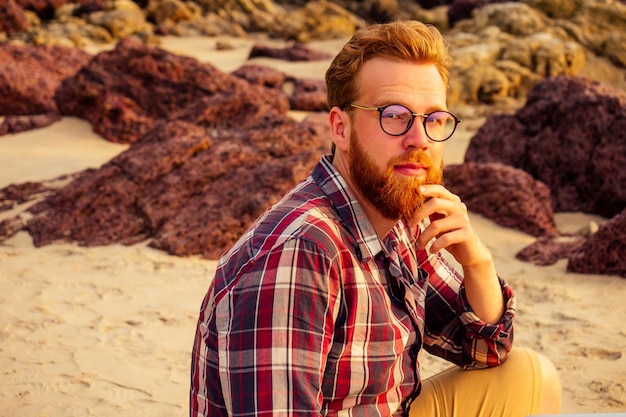 Pigiste masculin lunettes barbu hipster avec un ordinateur portable travail à distance sur la plage au coucher du soleil