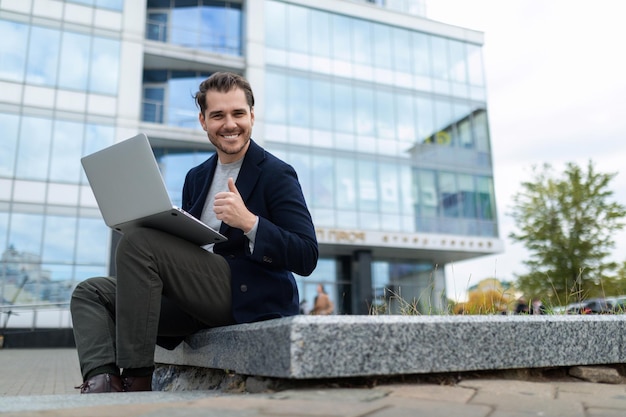 Un pigiste masculin avec un ordinateur portable sur le fond d'un immeuble de bureaux moderne regarde la caméra dans