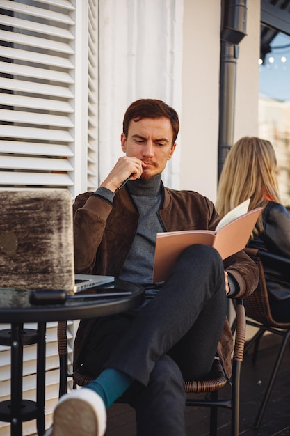 Pigiste masculin réfléchi avec ordinateur portable pensant à un projet tout en travaillant à distance dans un café