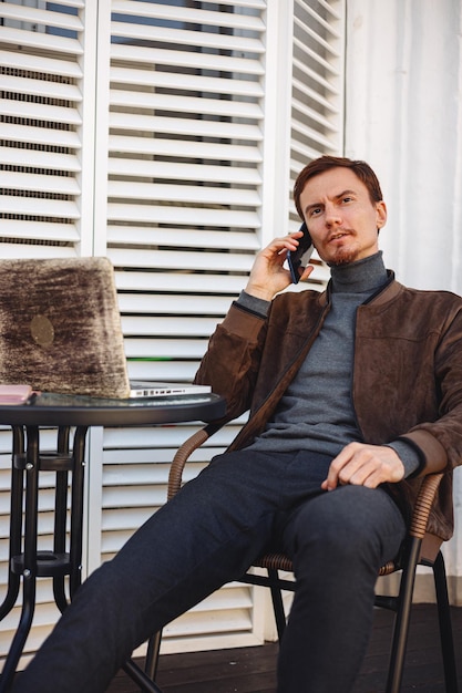 Pigiste masculin sérieux parlant au téléphone portable tout en étant assis dans un café en plein air