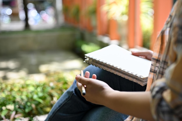 Une pigiste notant des idées dans un cahier tout en se relaxant est assise dans l'image recadrée du parc