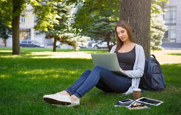 Pigiste occupé ou fille se préparant à entrer à l'université sur une herbe verte. Travailler avec un ordinateur portable dans le parc pendant la journée. Emploi indépendant à temps libre. Concept de mode de vie et de technologie