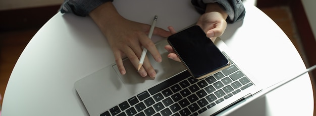 Pigiste à la recherche d'informations sur smartphone tout en travaillant avec un ordinateur portable sur une table basse