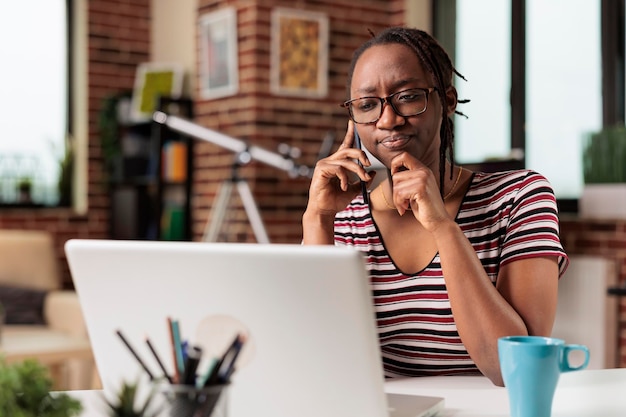 Pigiste réfléchi parlant sur smartphone avec le client, pensant à la solution, se frottant le menton, travaillant sur un ordinateur portable. Travailleur à distance occupé répondant à un appel téléphonique, employé ayant une conversation téléphonique