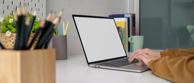 Pigiste travaillant à domicile avec un ordinateur portable à écran blanc sur une table de travail élégante avec des livres, de la papeterie et des décorations