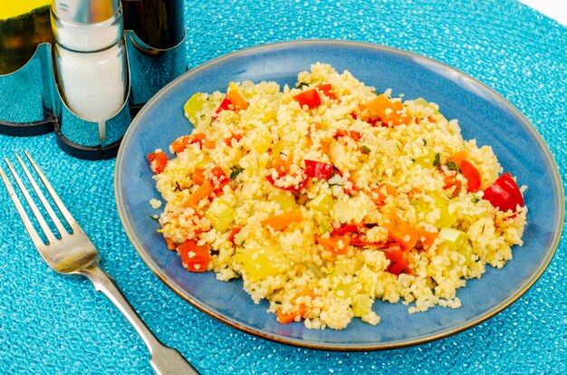 Pilaf de couscous végétarien aux légumes sur plaque bleue.