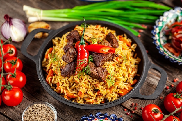 Pilaf national ouzbek avec de la viande dans une poêle en fonte, sur une table en bois.