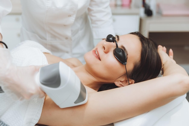 Épilation au laser des aisselles Cosmétologue enlevant les poils des aisselles d'une jeune femme Épilation au laser dans une clinique de beauté cosmétique Le concept de santé et de beauté