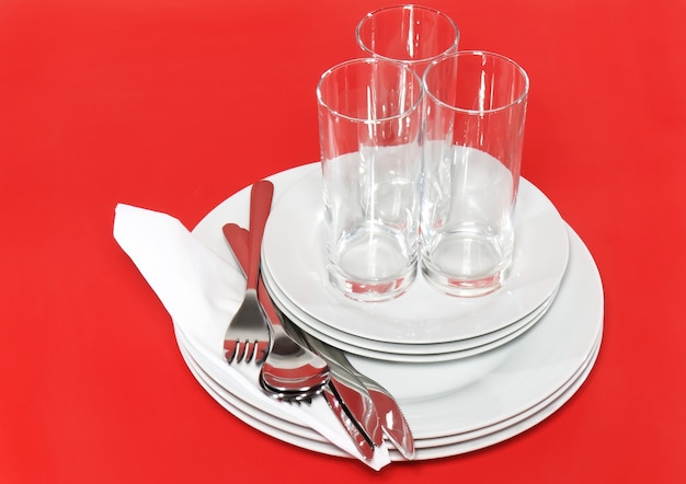 Photo pile d'assiettes blanches, verres avec fourchettes et cuillères sur serviette en soie. fond rouge