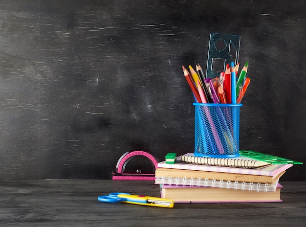 Pile de cahiers, verre bleu avec crayons en bois multicolores et stylo