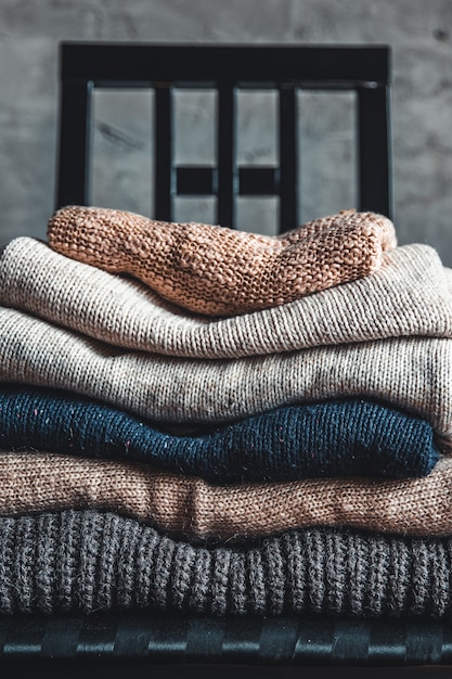 Une pile de chandails chauds et confortables tricotés, sur une chaise près du mur gris. automne, concept d'hiver.