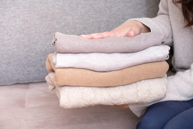 Pile de chandails tricotés confortables dans les mains des femmes sur fond de canapé Concept chaleureux