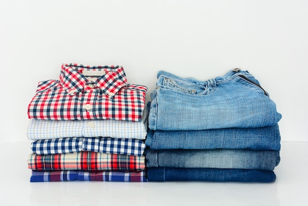 Pile de chemises et de jeans à carreaux colorés pliés sur fond blanc