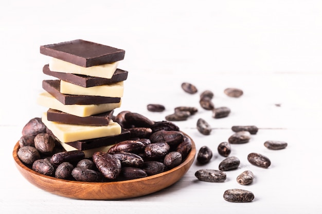 Pile de chocolat noir amer cru et de beurre de cacao avec des fèves de cacao sur une vieille table blanche rustique.