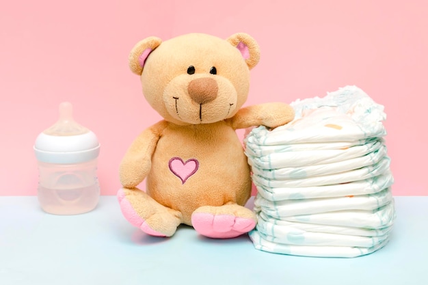 Pile de couches avec mignon nounours jouet bouteille de lait sur table pour bébé nouveau-né garçon fille pour cadeau de douche de bébé sur fond bleu rose Concept d'hygiène médicale de soins de santé