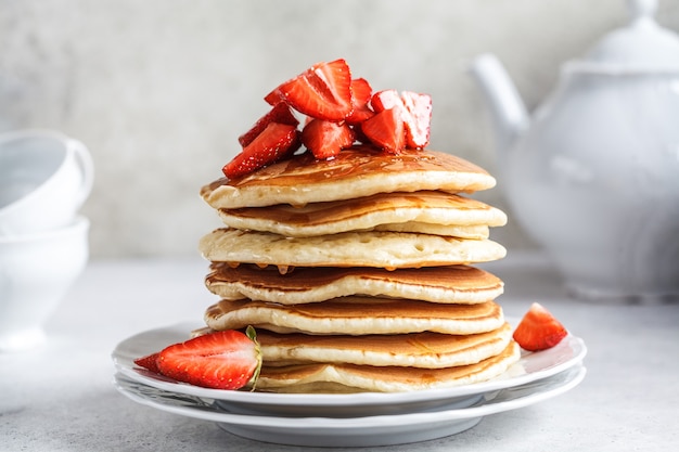 Pile de crêpes aux fraises et miel sur une plaque blanche.