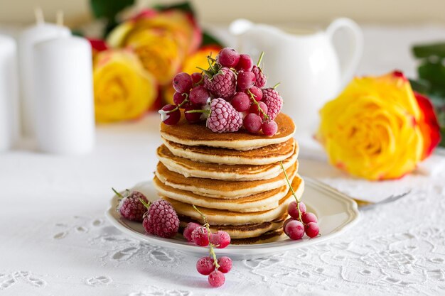 Une pile de crêpes avec de la crème de raisin rouge et du miel sur un drap de table blanc