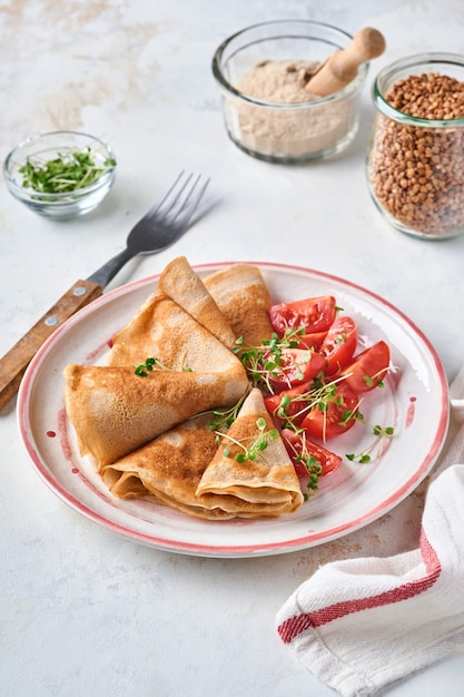 Pile de crêpes à la farine de sarrasin sans gluten avec tomates cerises et micro-pousses de roquette sur plaque blanche, cuisson saine maison pour le petit-déjeuner. Maquette. Espace de copie.