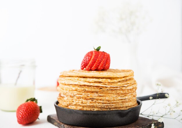 Une pile de crêpes maison aux fraises dans une poêle sur une surface blanche