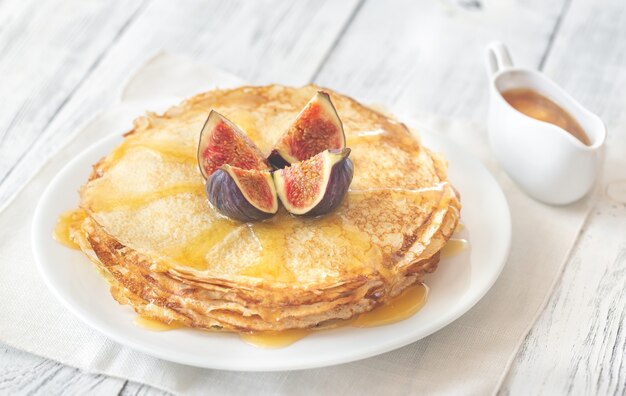 Pile de crêpes maison avec figues fraîches et garniture sucrée sur la plaque blanche