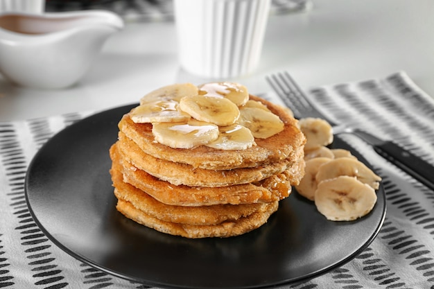 Pile de délicieuses crêpes à la noix de coco avec sauce sucrée et tranches de banane sur plaque, gros plan