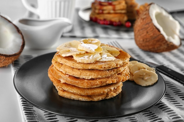 Pile de délicieuses crêpes à la noix de coco avec sauce sucrée et tranches de banane sur la table