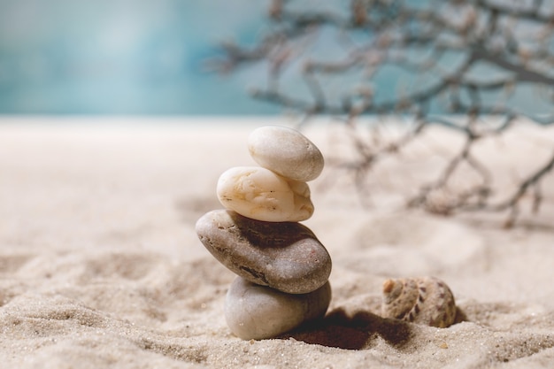 Pile de différentes pierres lisses blanches dans la composition d'équilibrage sur la plage de sable d'été avec des vagues et des coquillages. Copiez la disposition créative de l'espace. Concept d'équilibre de vacances.