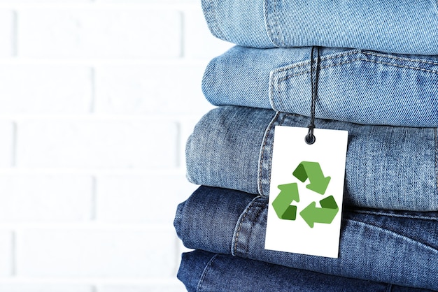 Pile de différents jeans avec étiquette de recyclage près du mur de briques blanches agrandi Espace pour le texte