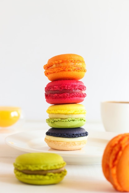 Pile de divers macarons sur la table avec des tasses de jus d'orange et de café dessert français