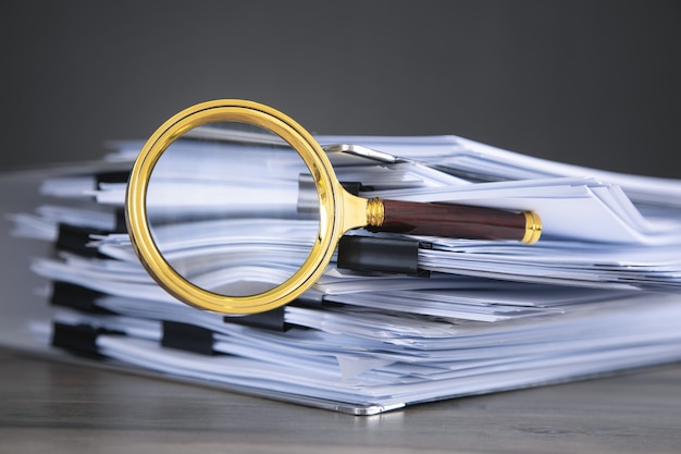 Pile de documents et loupe sur la table.