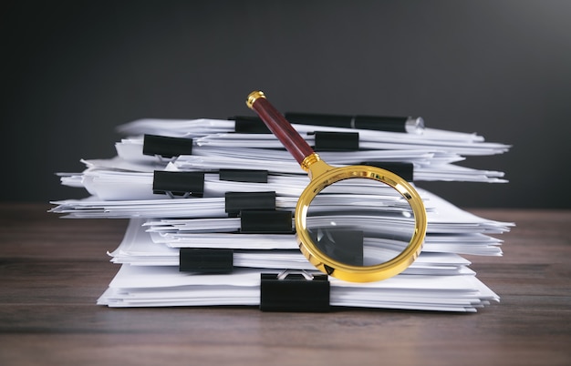 Pile de documents et loupe sur la table.