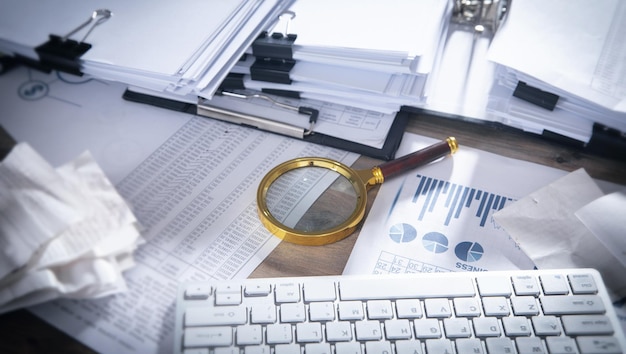 Pile de documents et loupe sur la table.