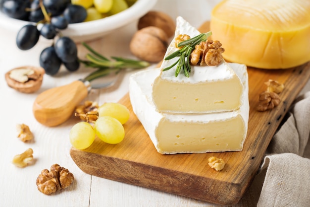 Pile de fromage camembert avec raisins, noix et basilic sur fond de béton ou de pierre gris clair