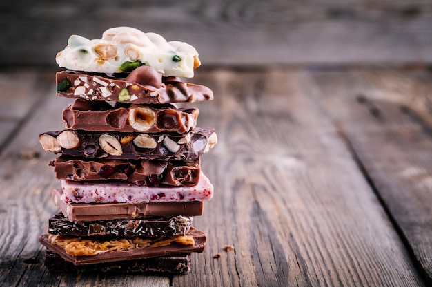 Pile de lait blanc et chocolat noir avec caramel aux noix et fruits et baies sur fond rustique en bois