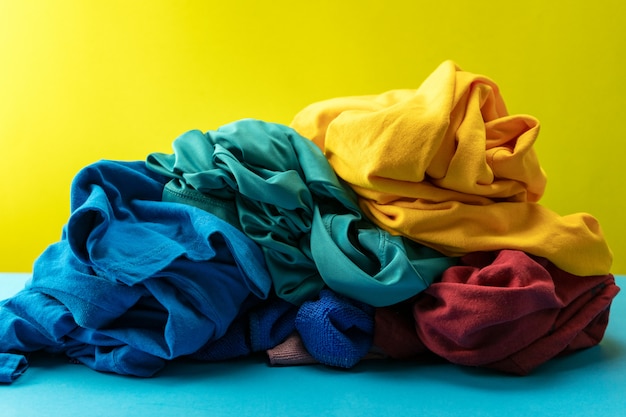 Pile de linge sale sur table bleue fond clair jaune.